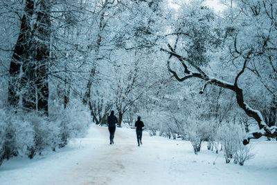 Rear view of people running on snow covered field