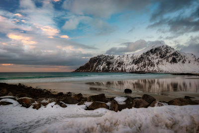 Scenic view of sea by snowcapped mountains against sky