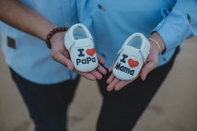 Midsection of couple holding baby booties with text