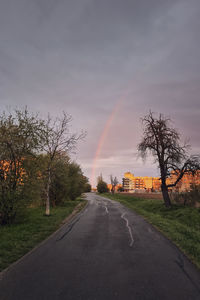 Road amidst plants and rainbow against sky during sunset