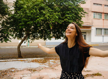 Cheerful woman with arms outstretched standing against building