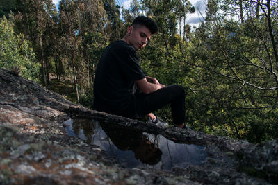 Side view of young man sitting in forest