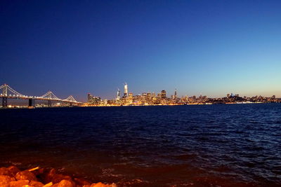 Illuminated city at waterfront against blue sky