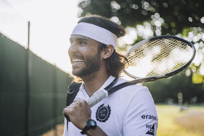 Happy man wearing headband looking away holding tennis racket