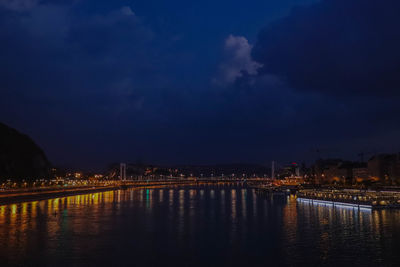 Illuminated buildings by river against sky at night