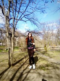 Full length of young woman standing by bare tree at park