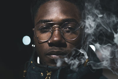 Close-up portrait of young man smoking at night