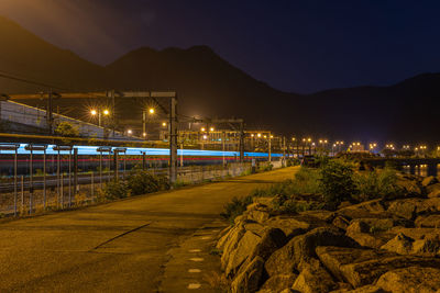 Illuminated street by mountain against sky at night