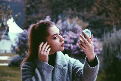 Young woman with handheld mirror outdoors