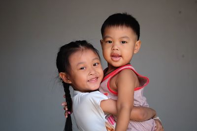 Portrait of cute girl carrying brother against wall
