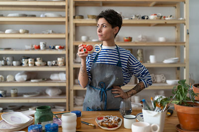 Creative ceramist woman in dirty apron enjoying her morning coffee from clay mug and looking away