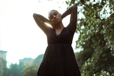 Low angle view of woman standing by tree against sky