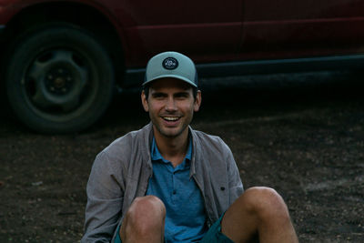 Portrait of smiling young man sitting against car