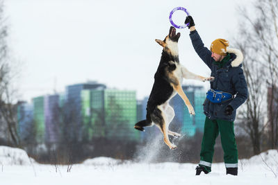 Man playing with dog in snow against sky