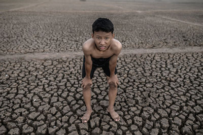 Portrait of shirtless boy standing on cracked land