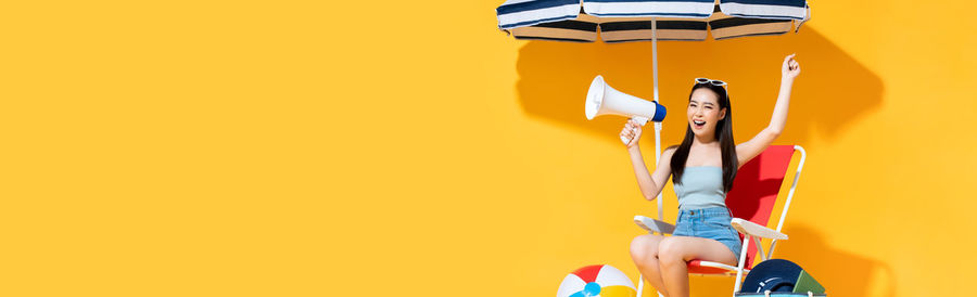 Woman holding umbrella against yellow background