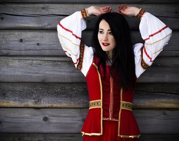 Thoughtful young woman wearing traditional clothing against wooden wall