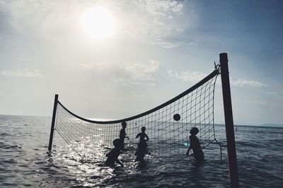 Silhouette people playing beach volleyball against sky during sunset