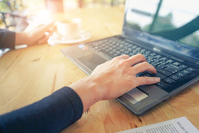 Cropped hands of woman using laptop on table