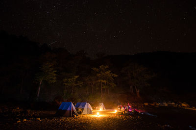 Illuminated lighting equipment by tents against sky at night