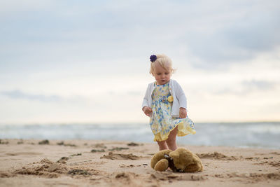 Girl with stuffed toy at beach against sky