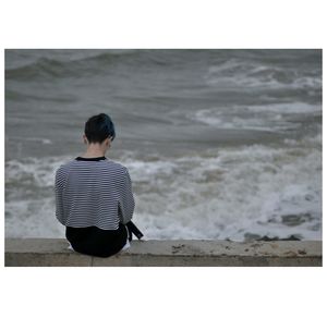 Rear view of man sitting on retaining wall against sea