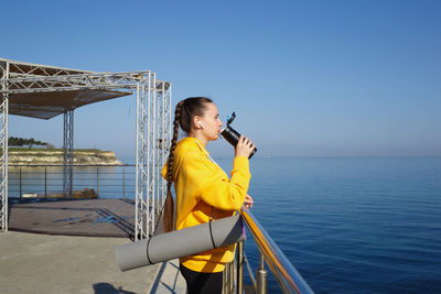 Young woman using mobile phone by sea against clear sky