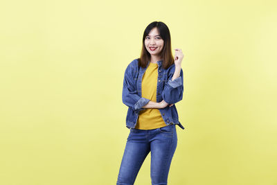 Portrait of smiling young woman against yellow background