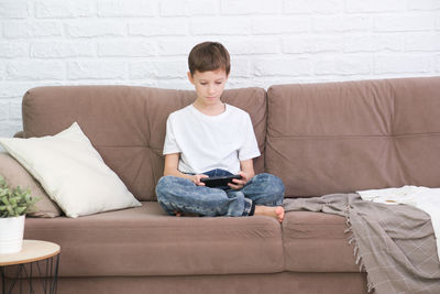 Boy using phone while sitting on sofa at home