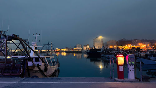 Sailboats moored at harbor against foggy sky at night