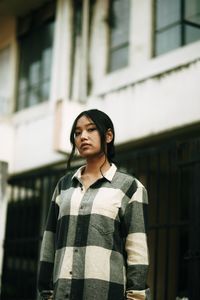 Portrait of young woman standing against building