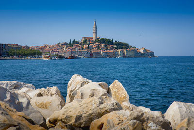 Scenic view of sea by buildings against clear blue sky