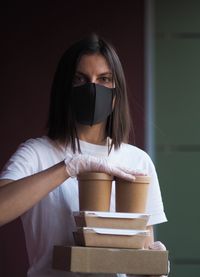 Portrait pretty delivery woman with dark shair in protective mask holding to delivery boxes.