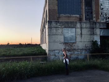 Woman standing by building against sky during sunset