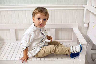 Portrait of a child boy two years old sitting on a wooden bench in a white studio