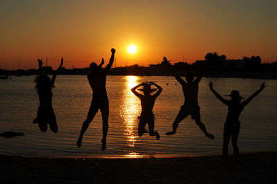 Silhouette friends jumping at beach against sky during sunset