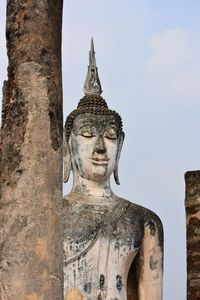 Low angle view of weathered buddha against sky