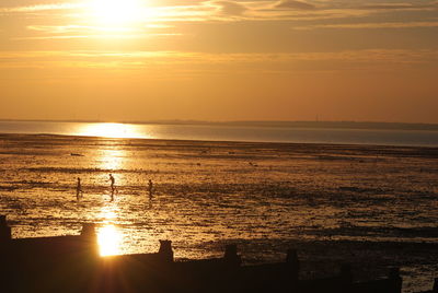 Silhouette people at beach against sky during sunset