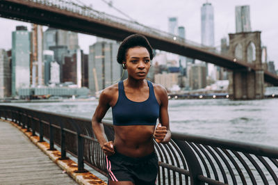 Portrait of young woman standing on footbridge in city