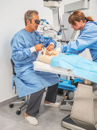 Side view of adult man and woman in medical uniform examining and preparing little dog to surgery with anesthesia while working in modern vet clinic