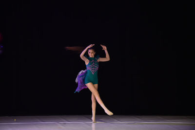 Full length of woman dancing against black background