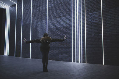 Full length of woman holding equipment while standing against illuminated lights on wall