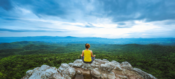 Rear view of woman sitting on rock against sky