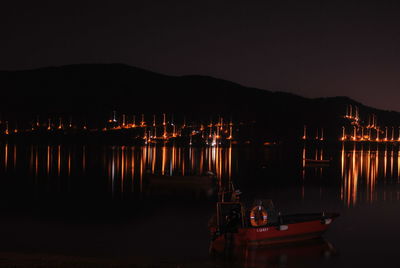 Illuminated boats moored at harbor against clear sky at night