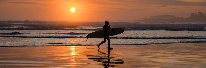 Low angle view of silhouette woman standing at beach against sky during sunset