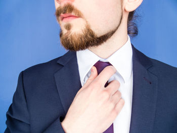 Midsection of businessman adjusting tie against blue background