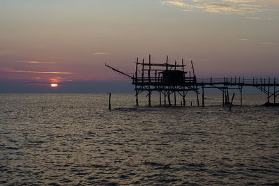 Silhouette pier over sea against sky during sunset