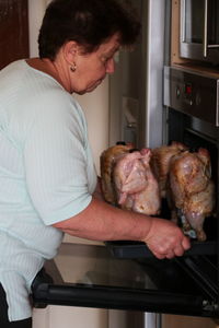 Side view of woman preparing meat in oven at home