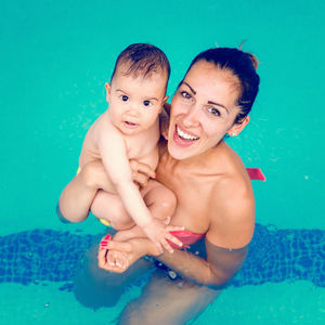 High angle portrait of mother carrying toddler son in pool