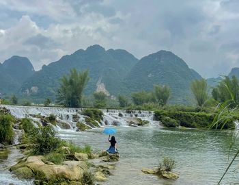 Woman in river by mountains against sky